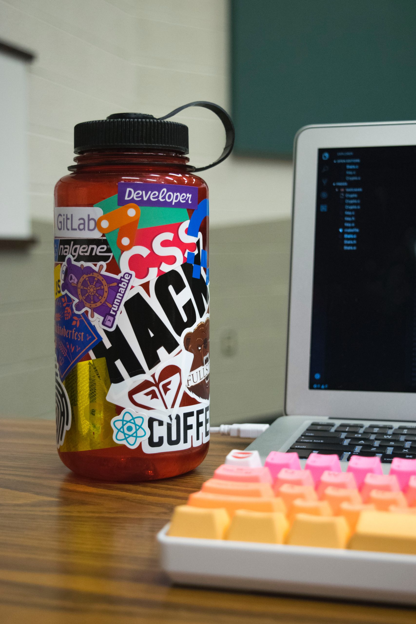 a water bottle covered in stickers beside a laptop.