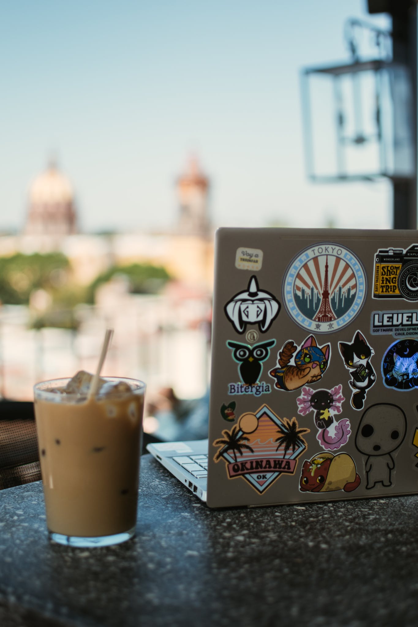a laptop covered in stickers next to an iced coffee on a table.