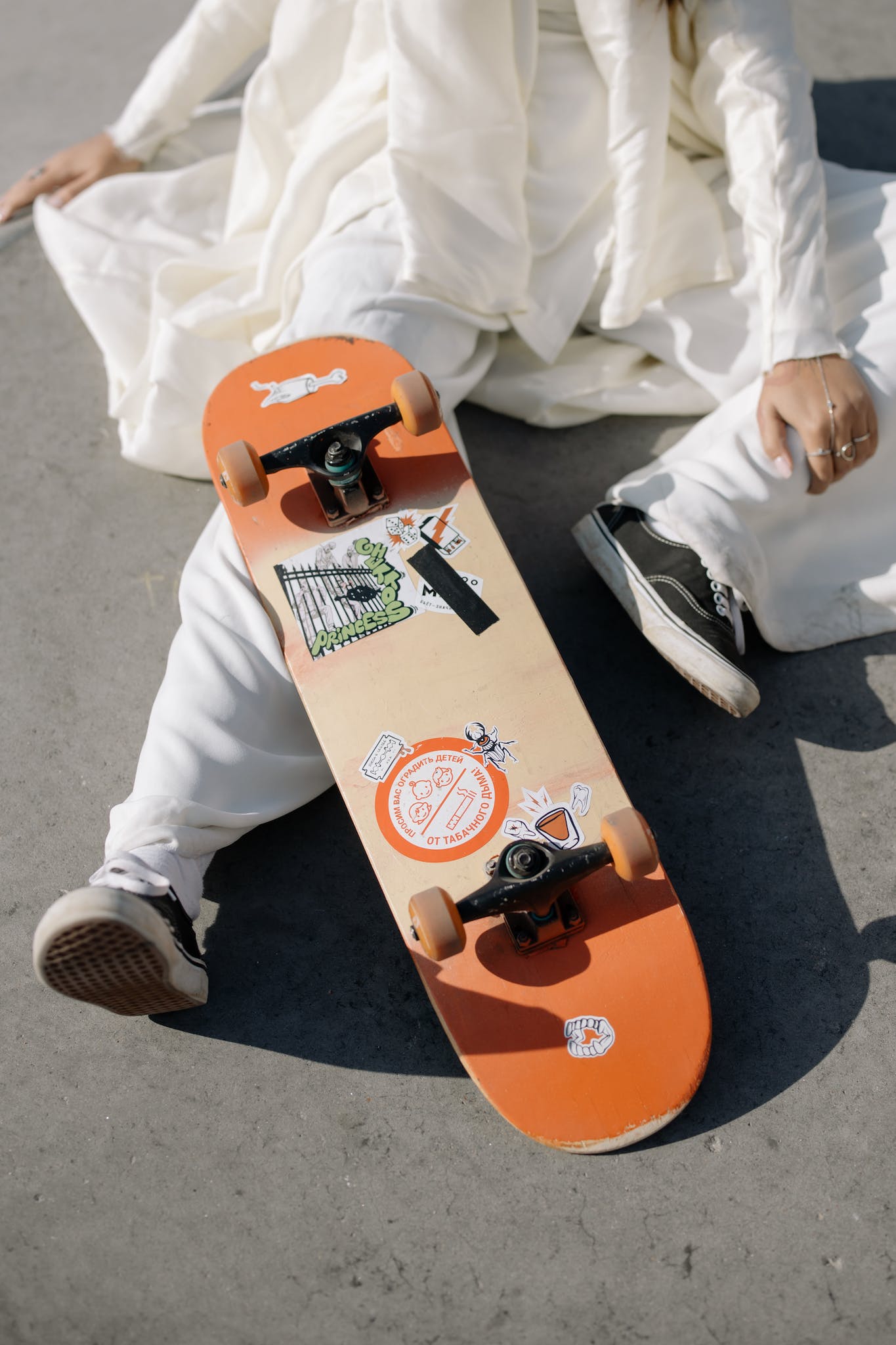 Person Sitting on the Ground with an orange upside down skateboard on their leg, covered in stickers.